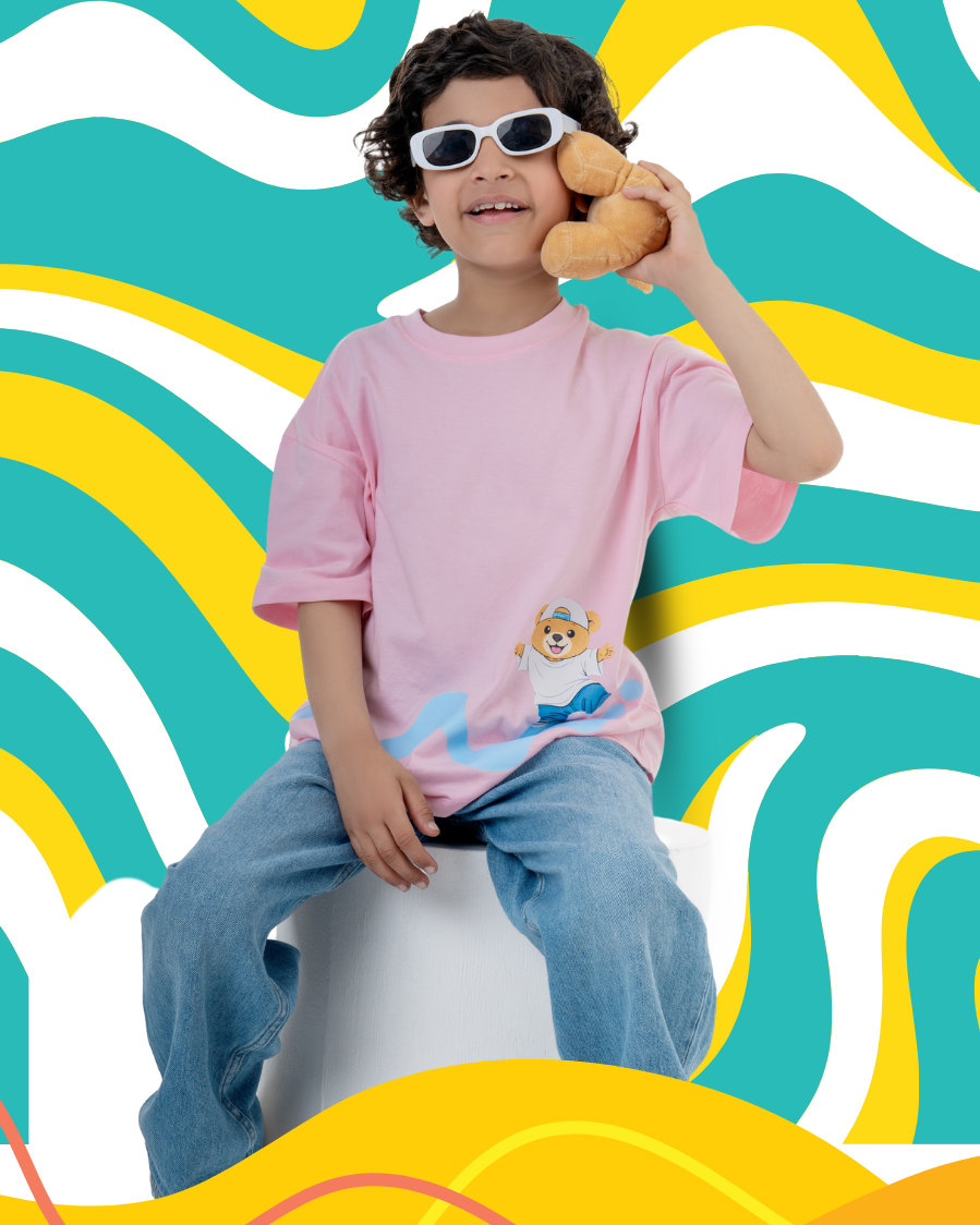 Child wearing a pink shirt with a teddy bear design, sitting on a white stool against a colorful wavy background.